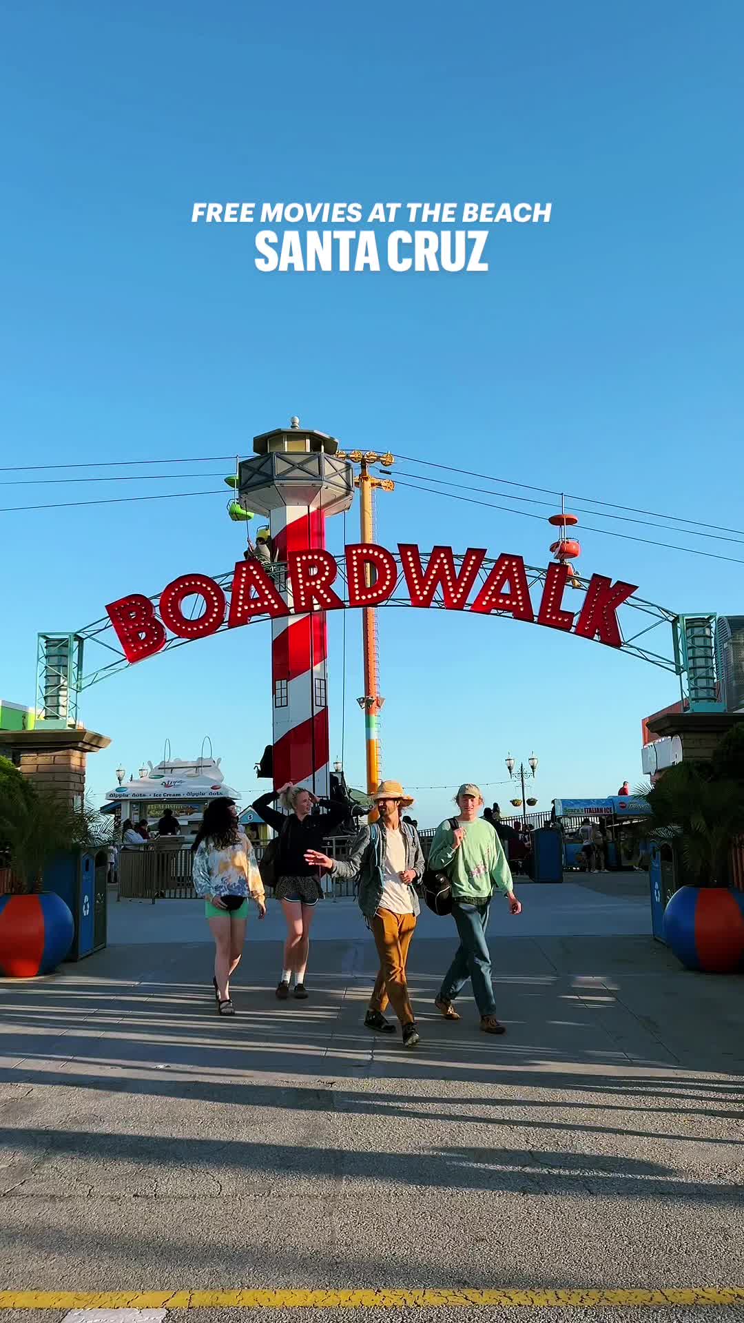 This may contain: people walking under a sign that says board walk on the side of the road in santa cruz, california