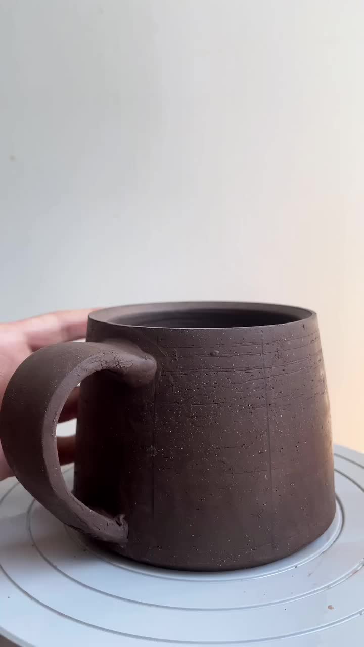 This may contain: two mugs sitting on top of a wooden table next to each other, one is made out of clay