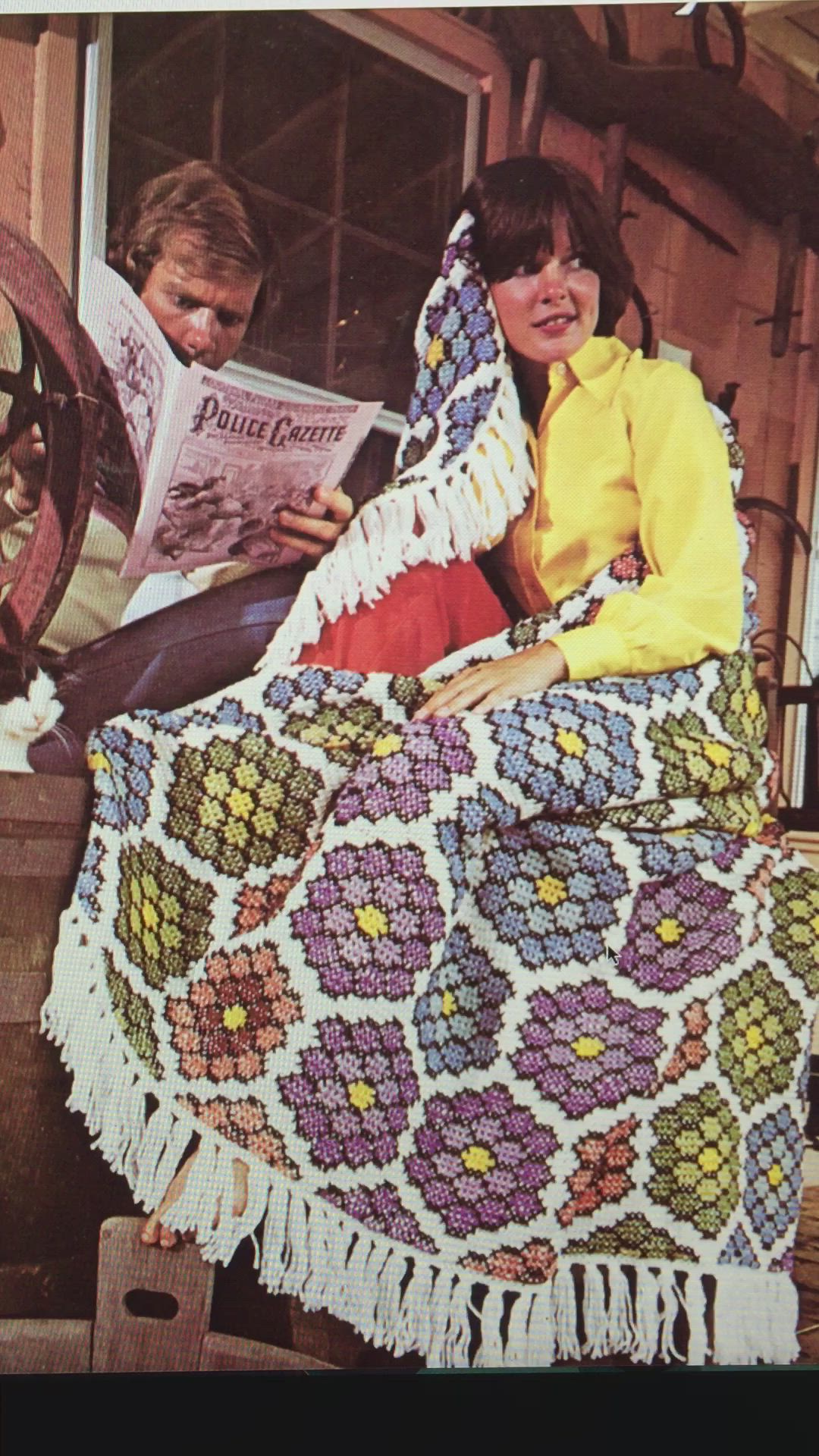 This may contain: a man and woman sitting on a porch with a blanket over their heads, reading a magazine