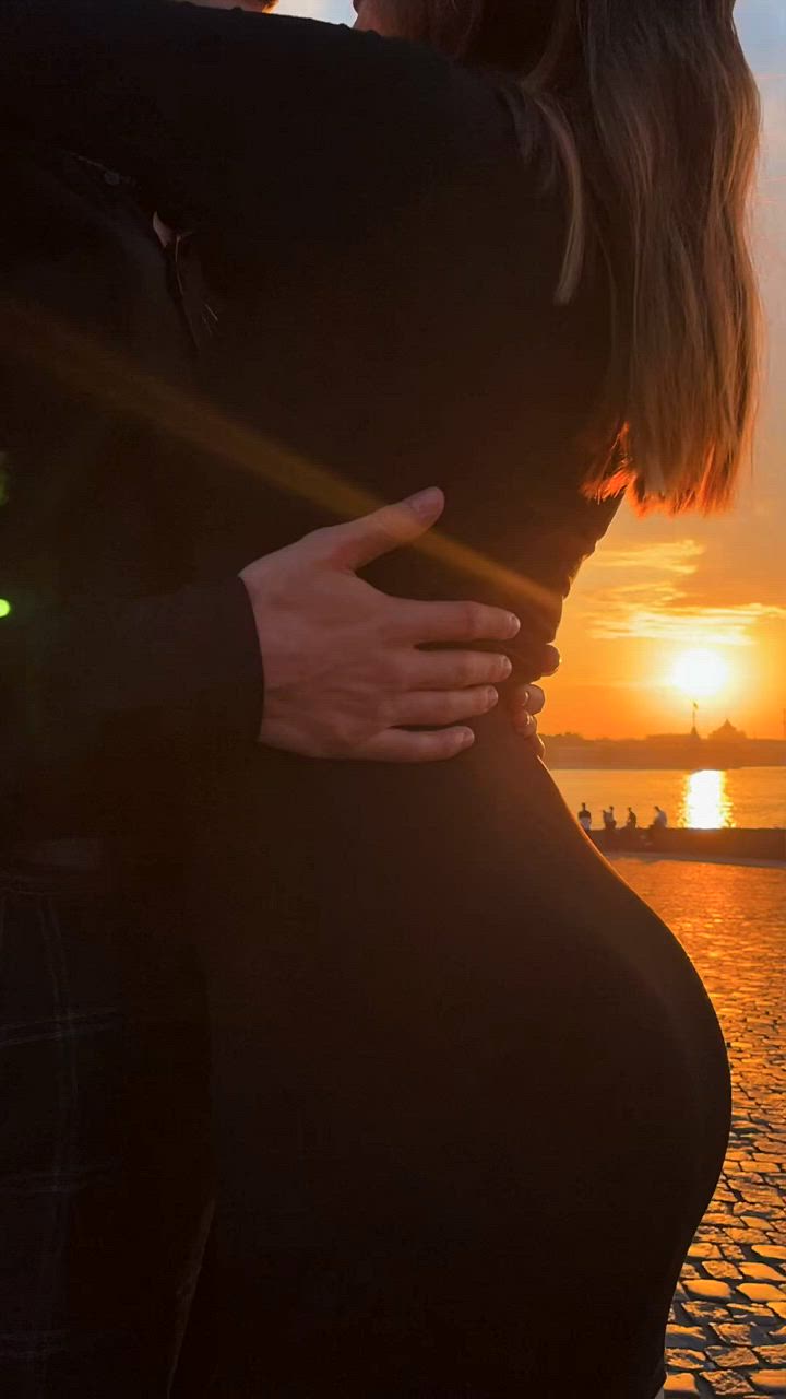 This may contain: two people standing next to each other in front of the ocean at sunset or sunrise