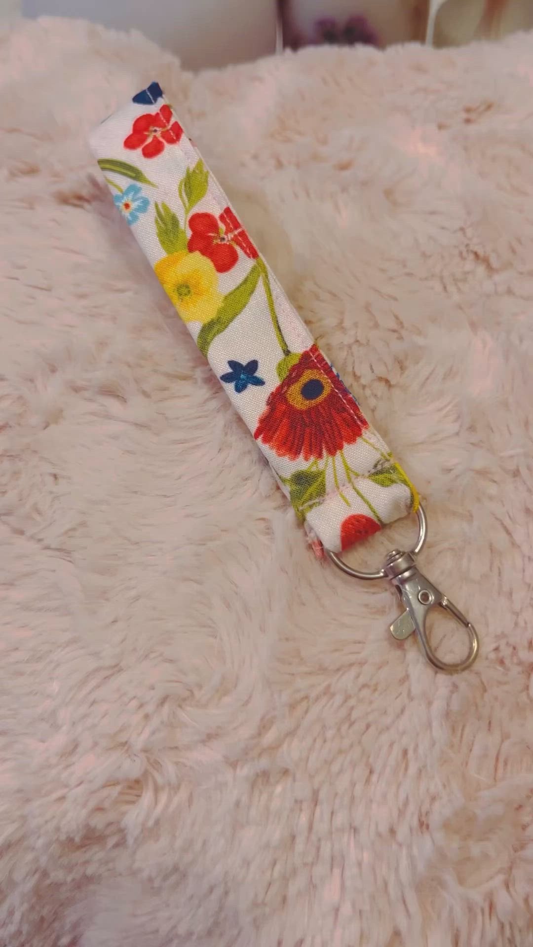 This may contain: a keychain with flowers on it sitting on top of a fluffy white blanket