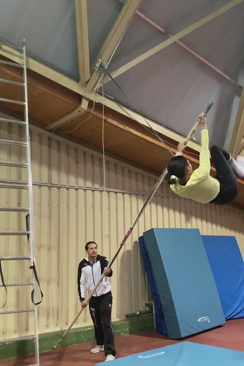 This may contain: a man is doing tricks on a pole in an indoor gym while another man watches