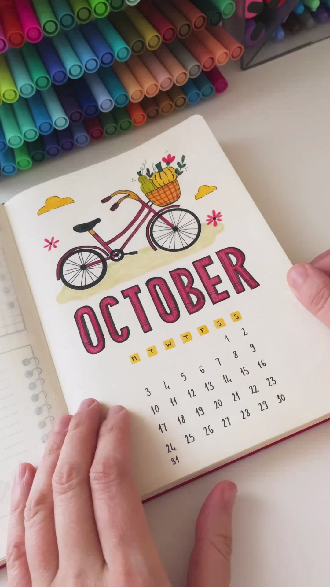 This may contain: a person holding a calendar with the word october written on it in front of colored crayons