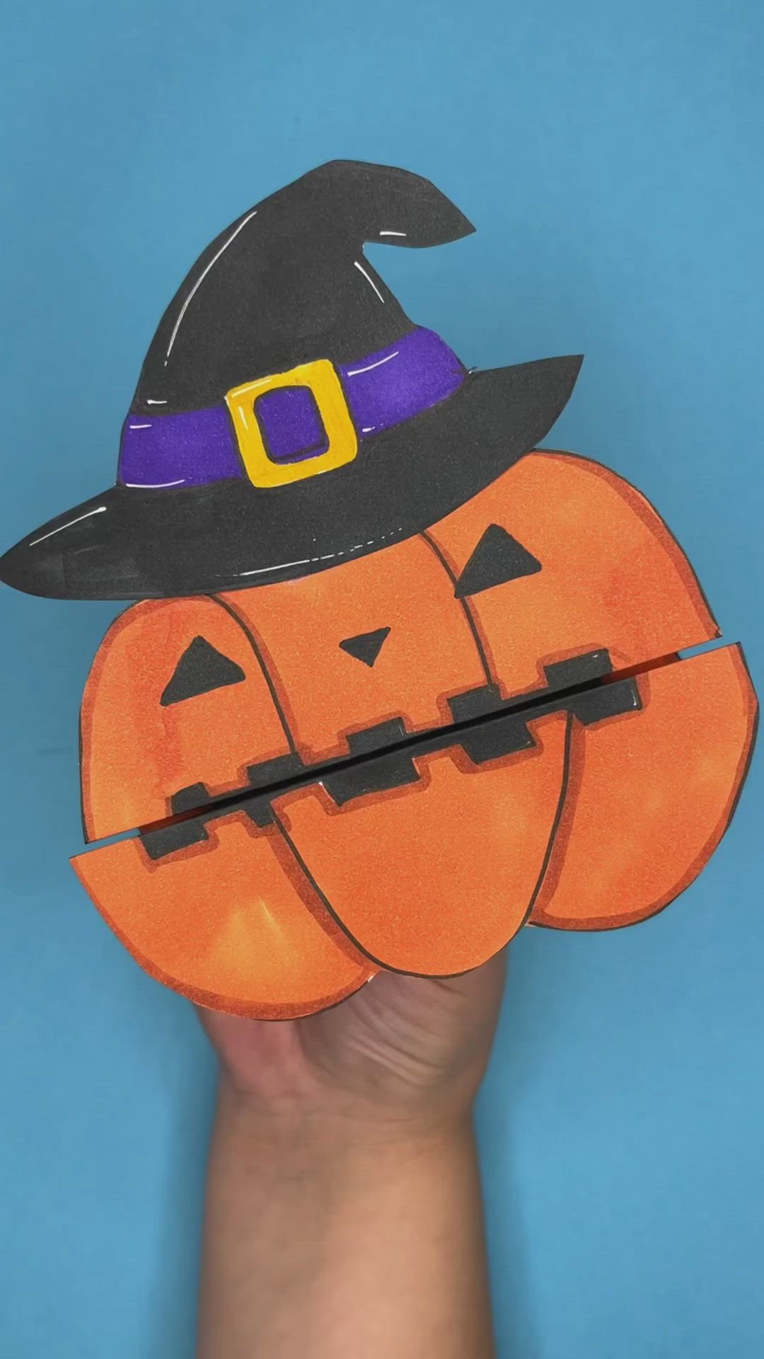 This may contain: a hand holding an orange paper pumpkin with a witch hat on it