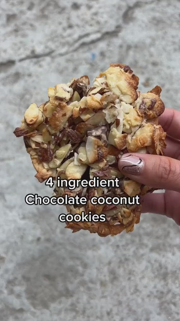 This may contain: a person holding up a cookie with chocolate and nuts on it that reads, 4 ingredient chocolate coconut cookies