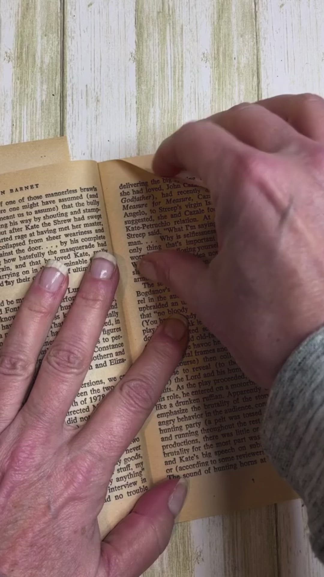 This may contain: an older person is reading a book with their hands on the open book and pointing at it