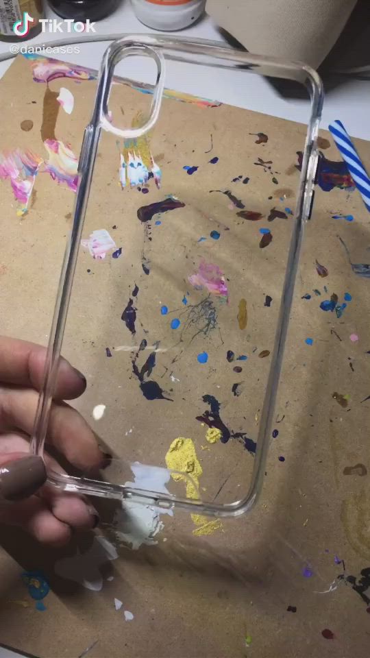 This may contain: a person holding up a cell phone case with black and yellow paint on it in front of a street