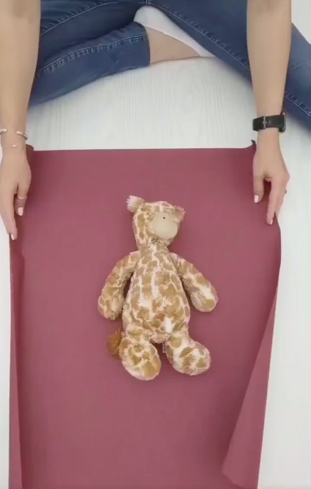 This may contain: a person holding a stuffed animal on top of a pink sheet with giraffe print