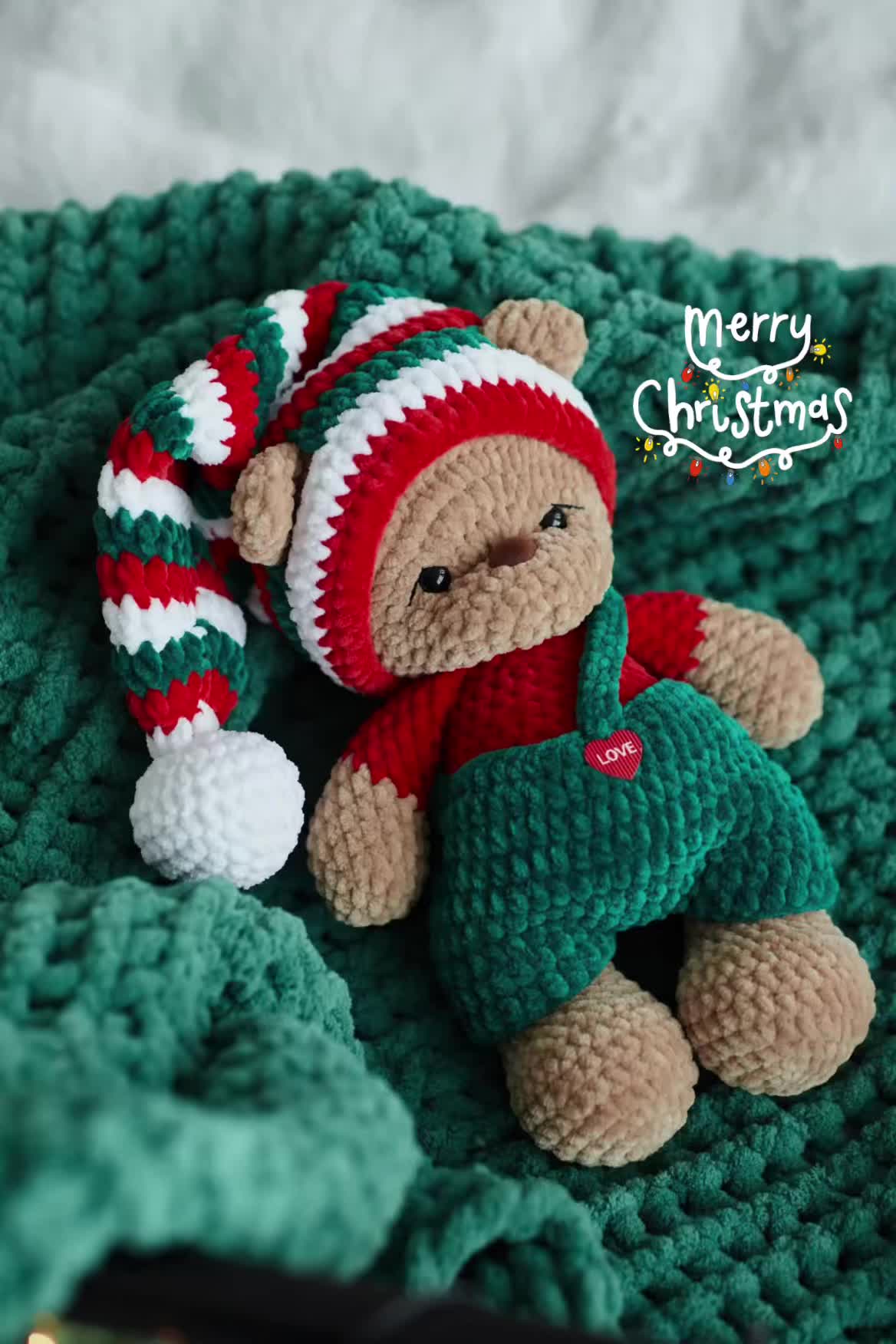 This may contain: a teddy bear laying on top of a green blanket next to a red and white christmas hat