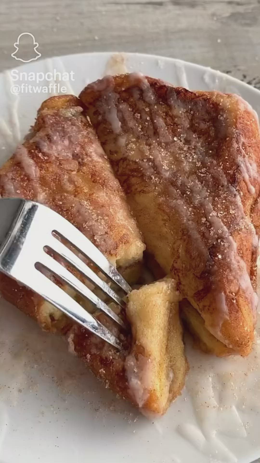 This may contain: a piece of french toast on a white plate with a fork in it and the words cinnamon roll brioche french toast