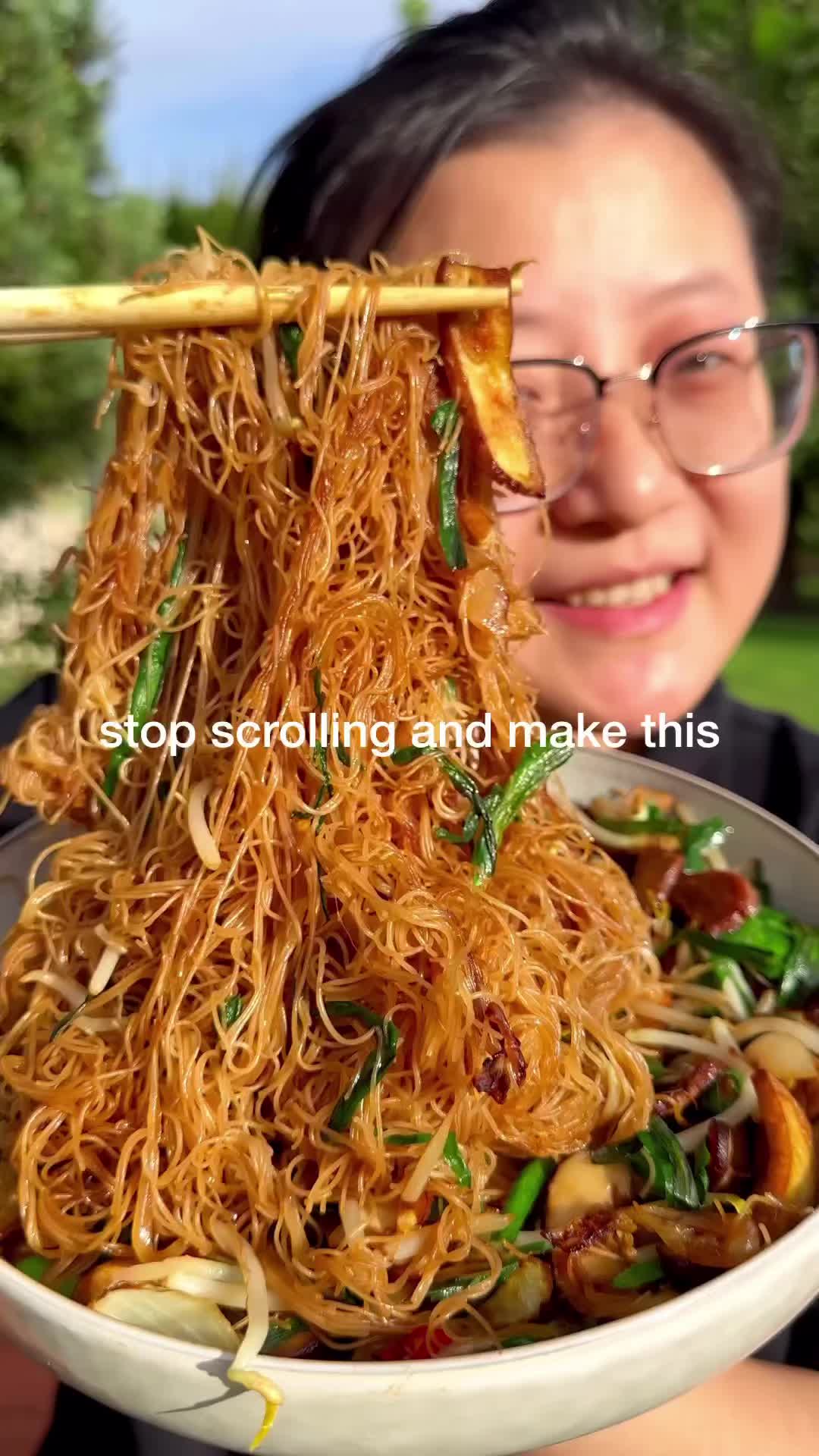 This may contain: a woman holding a bowl of noodles with chopsticks