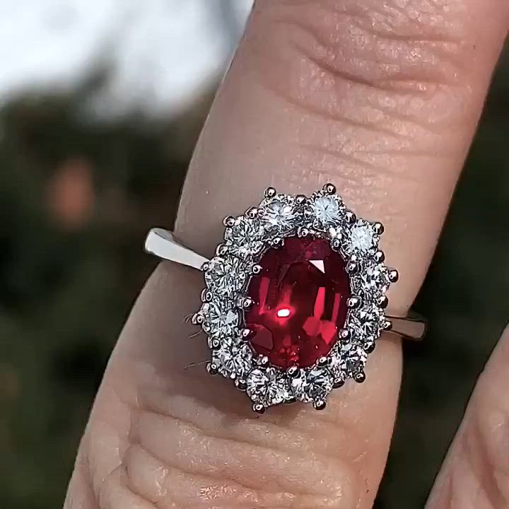 This may contain: a woman's engagement ring with an oval shaped red stone surrounded by white diamonds