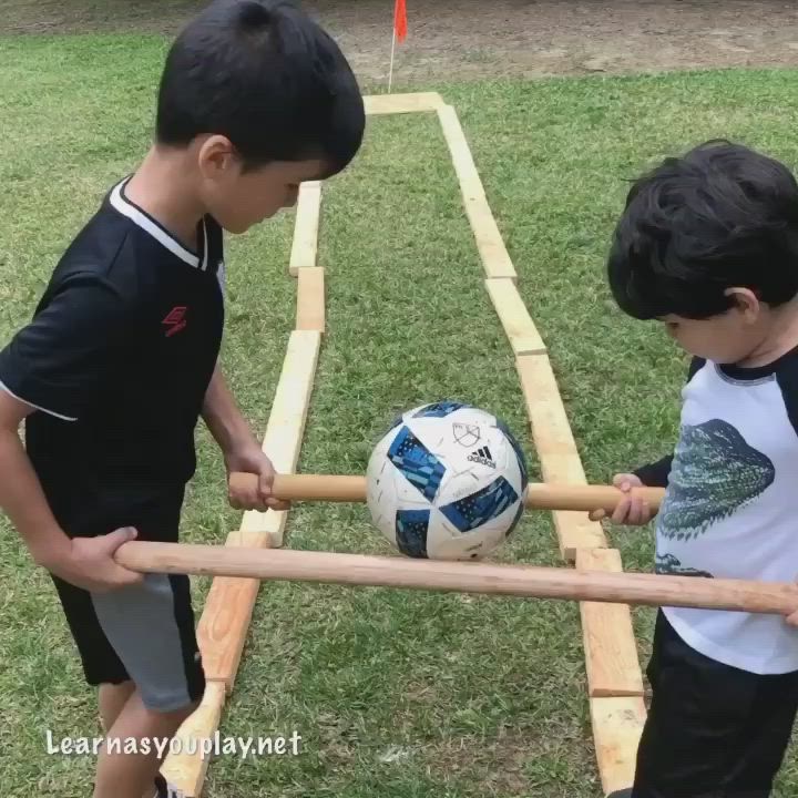 This may contain: two young boys playing with a soccer ball on a wooden frame in the grass outside