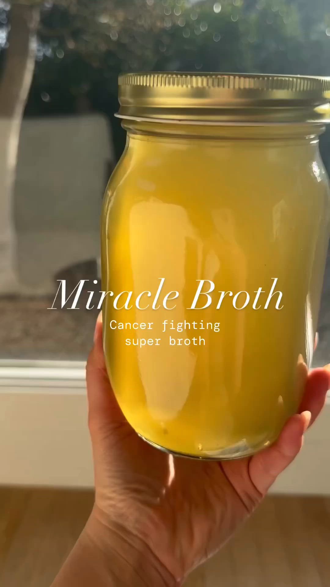 This may contain: a hand holding a jar filled with yellow liquid and the words, miracle broth