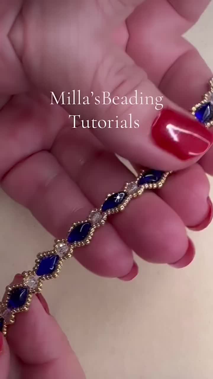 This may contain: a woman's hand with red nails holding a gold and blue beaded bracelet