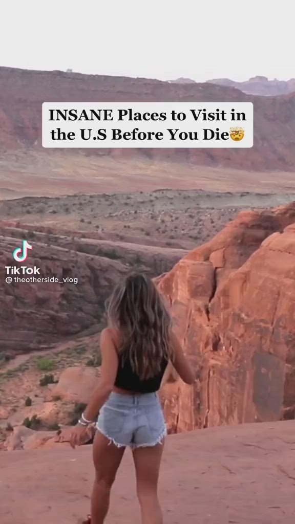 This may contain: a woman standing on top of a mountain next to a cliff with the caption insane places to visit in the u s before you die