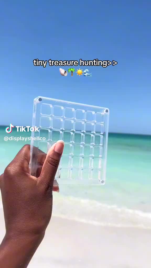 This may contain: a hand holding up a clear plastic case on top of a sandy beach next to the ocean