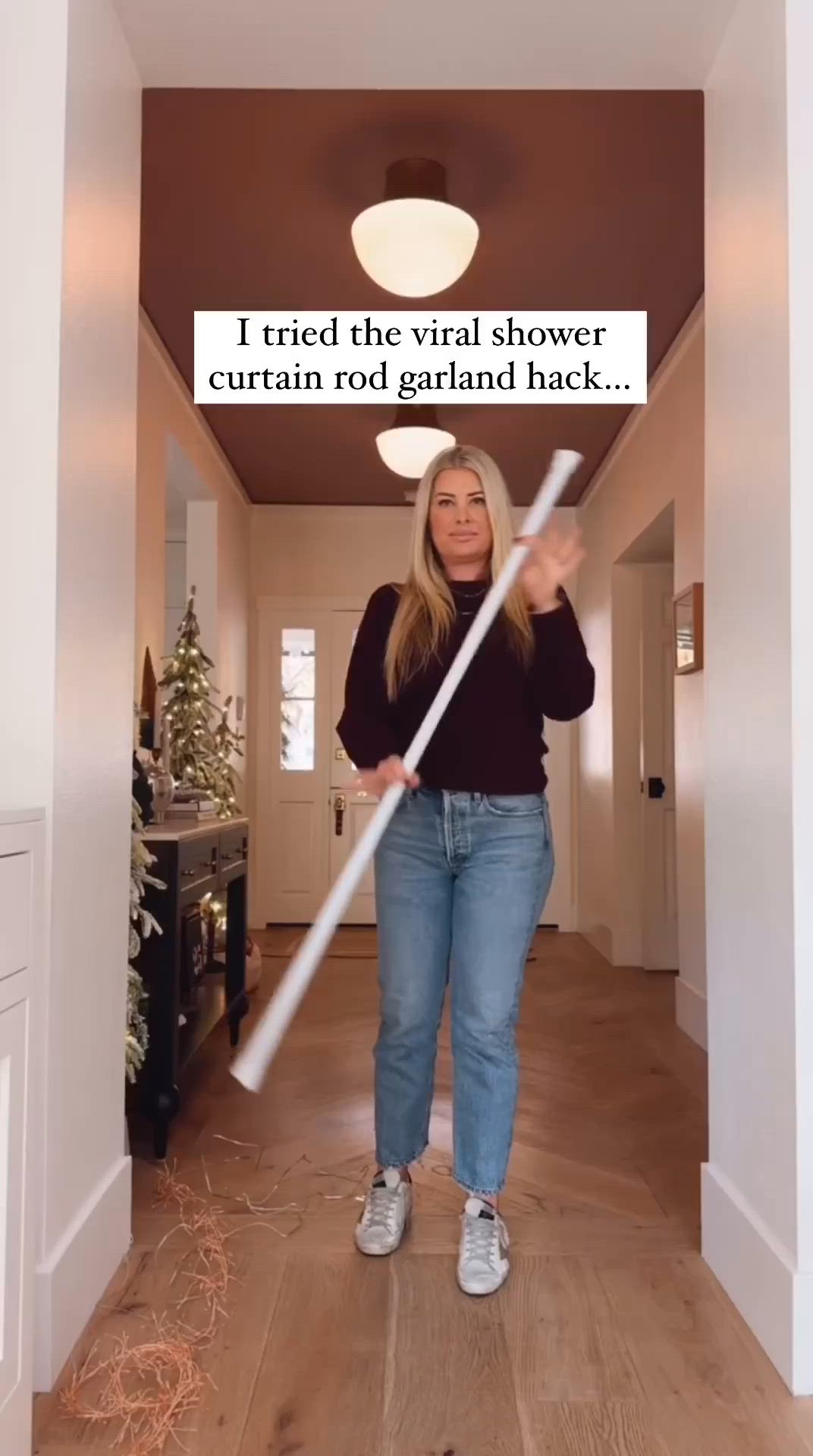 This may contain: a woman standing in a hallway holding a large white stick with the words i tried the virtual shower curtain curtain rod garland back