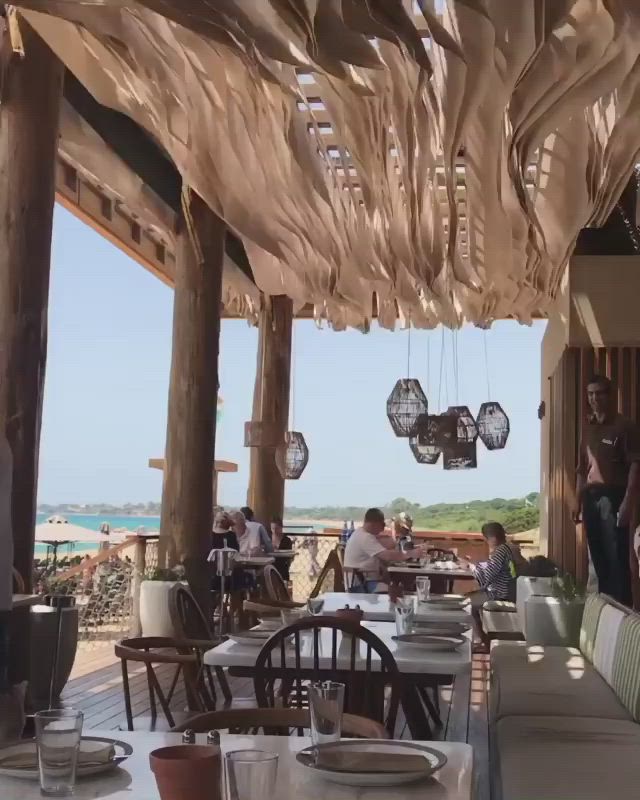 This may contain: an outdoor restaurant with tables and chairs on the beach