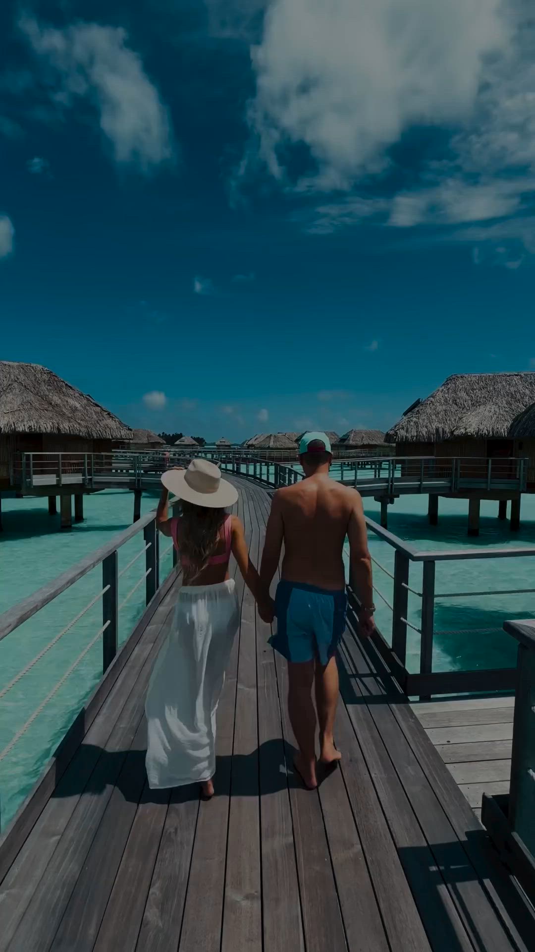 This may contain: a man and woman walking down a pier towards the ocean