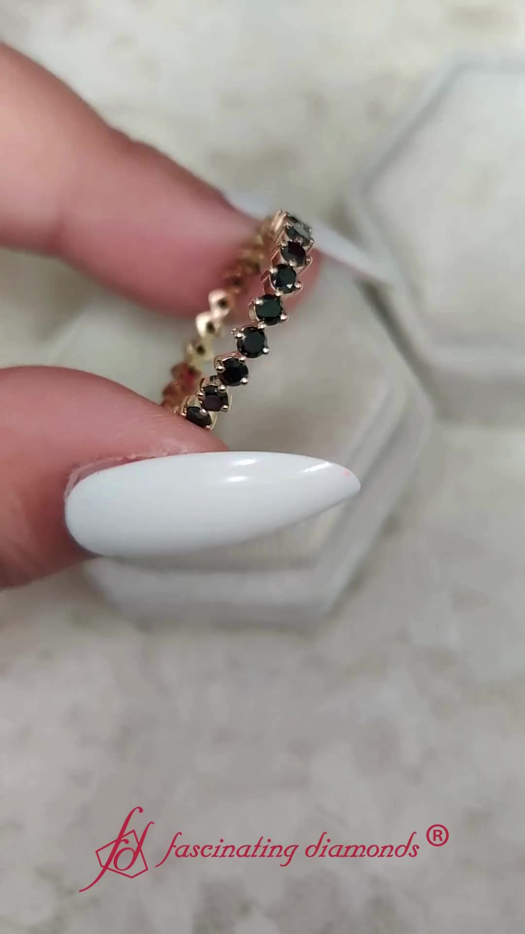 This may contain: a woman's hand with white and black nail polish holding a gold chain ring