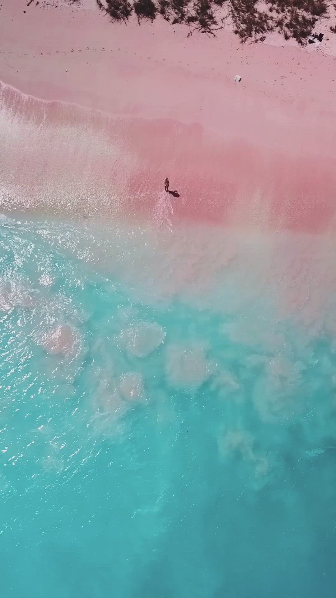 This may contain: a person riding a surfboard on top of a pink and blue body of water