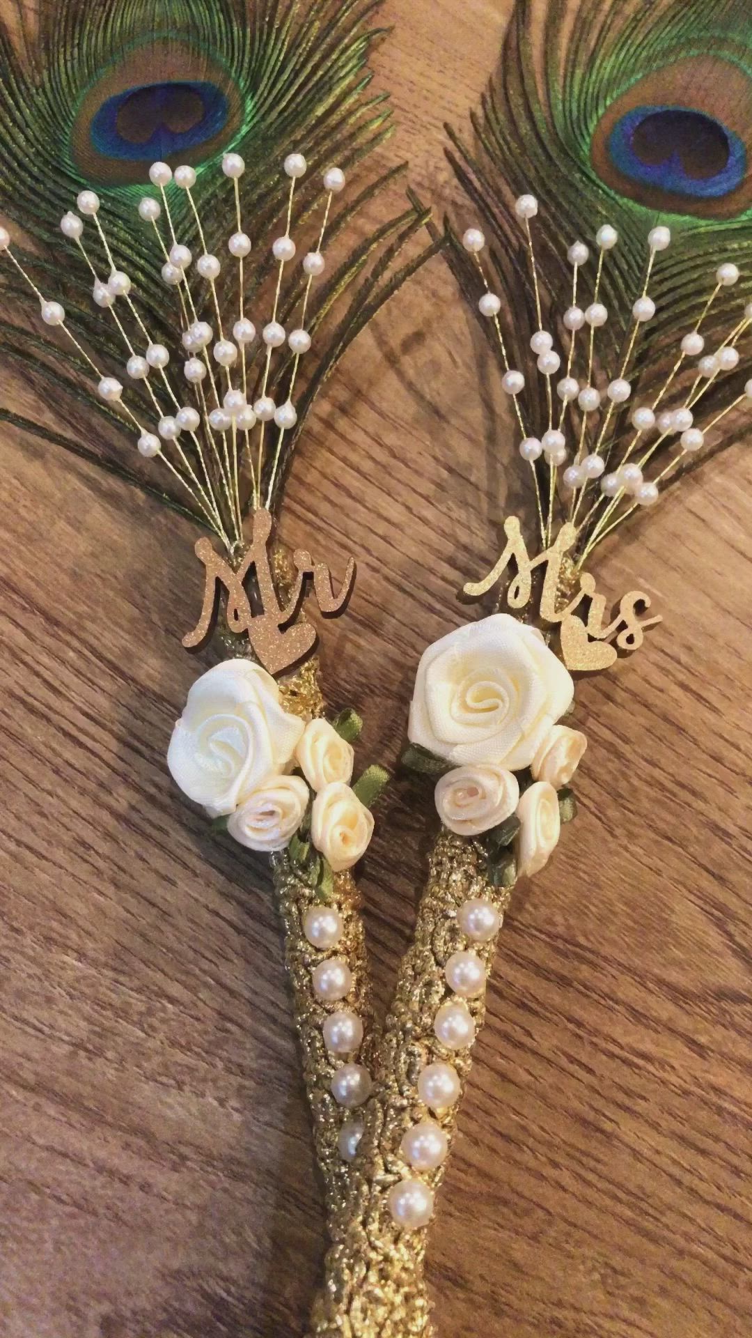 This may contain: two peacock feathers with white flowers and pearls on the stems, one is holding a monogram