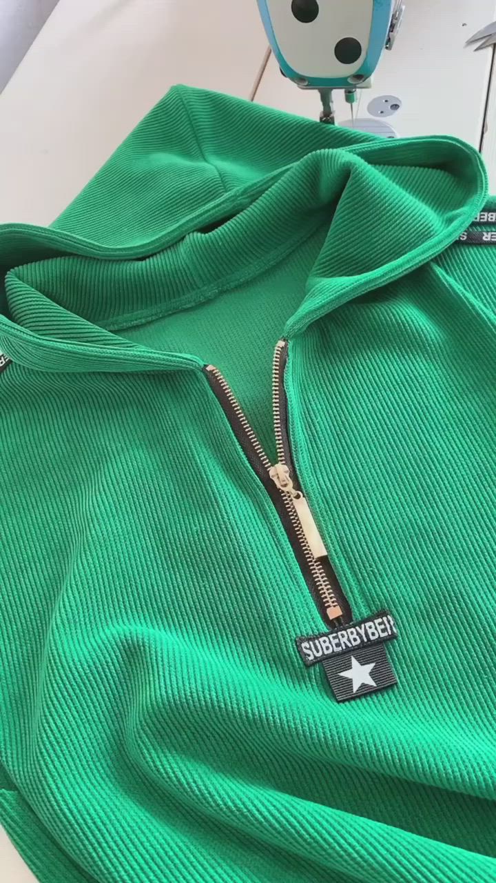 This may contain: a close up of a green hoodie on a white surface with a robot in the background