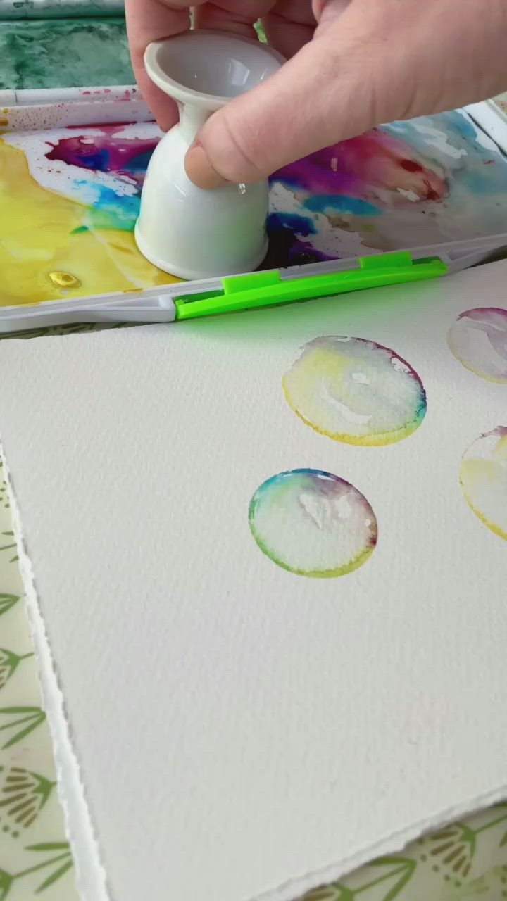 This may contain: a person is painting with watercolors on paper and using a glue pen to paint circles