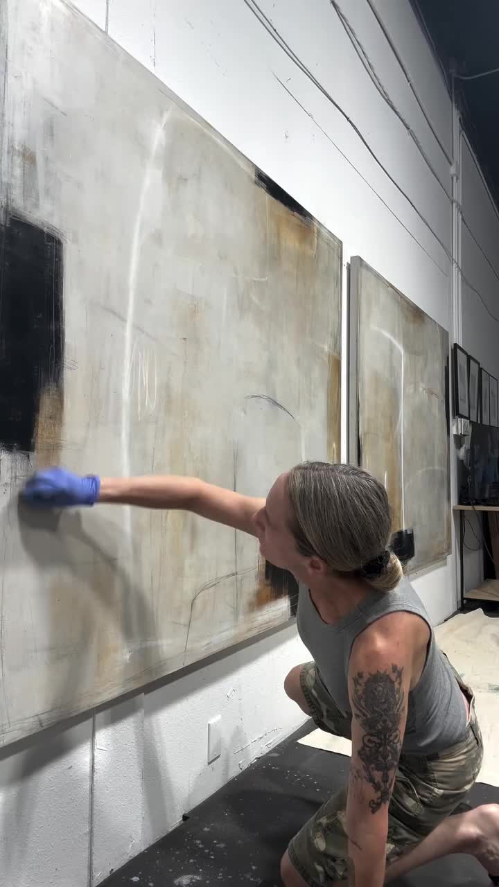 This may contain: a woman in grey shirt painting on wall with black and white paint, while wearing blue gloves