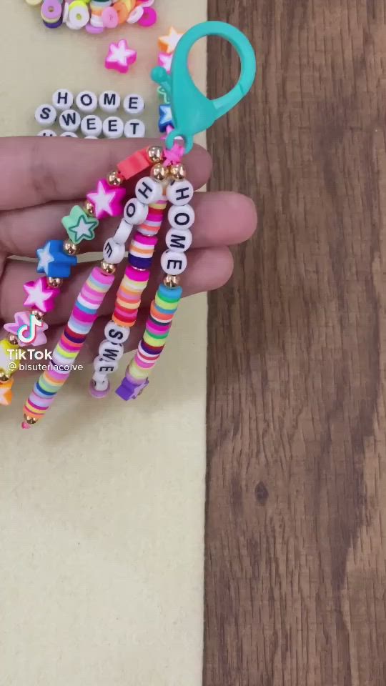 This may contain: a person holding some colorful beads on their finger and an item that says home sweet