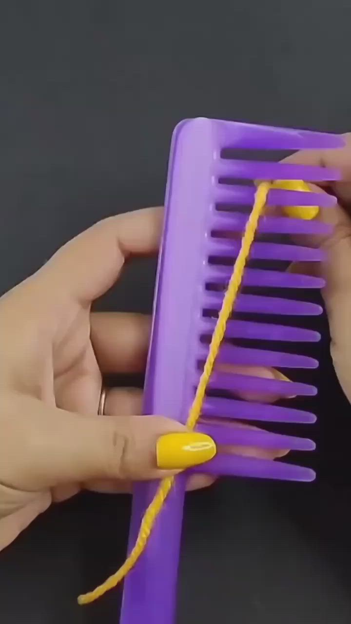 This may contain: two hands are holding a purple comb with yellow nails on it and one hand is pulling the comb out