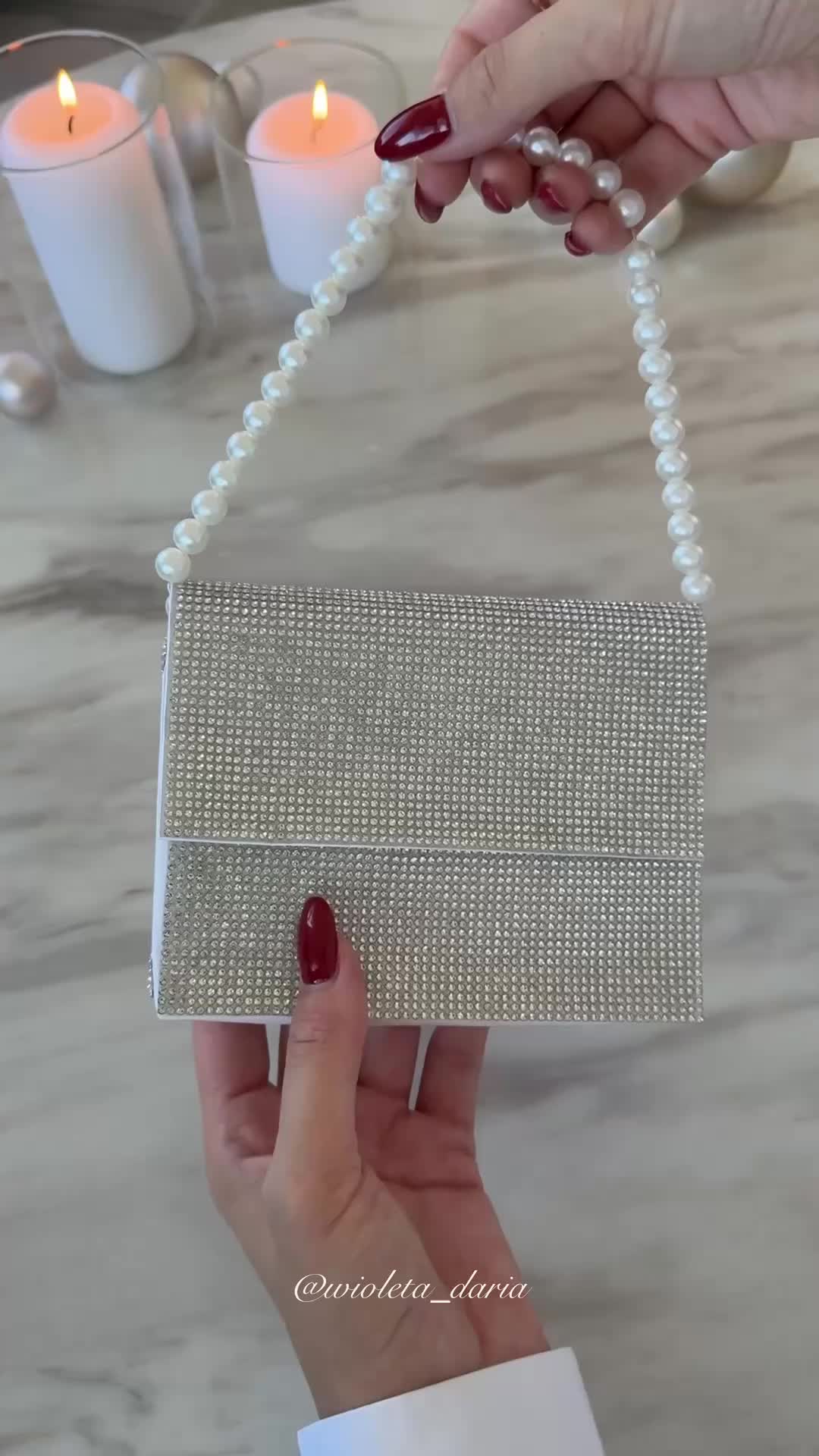 This may contain: a woman holding a white beaded purse with pearls on the handle and chain attached to it