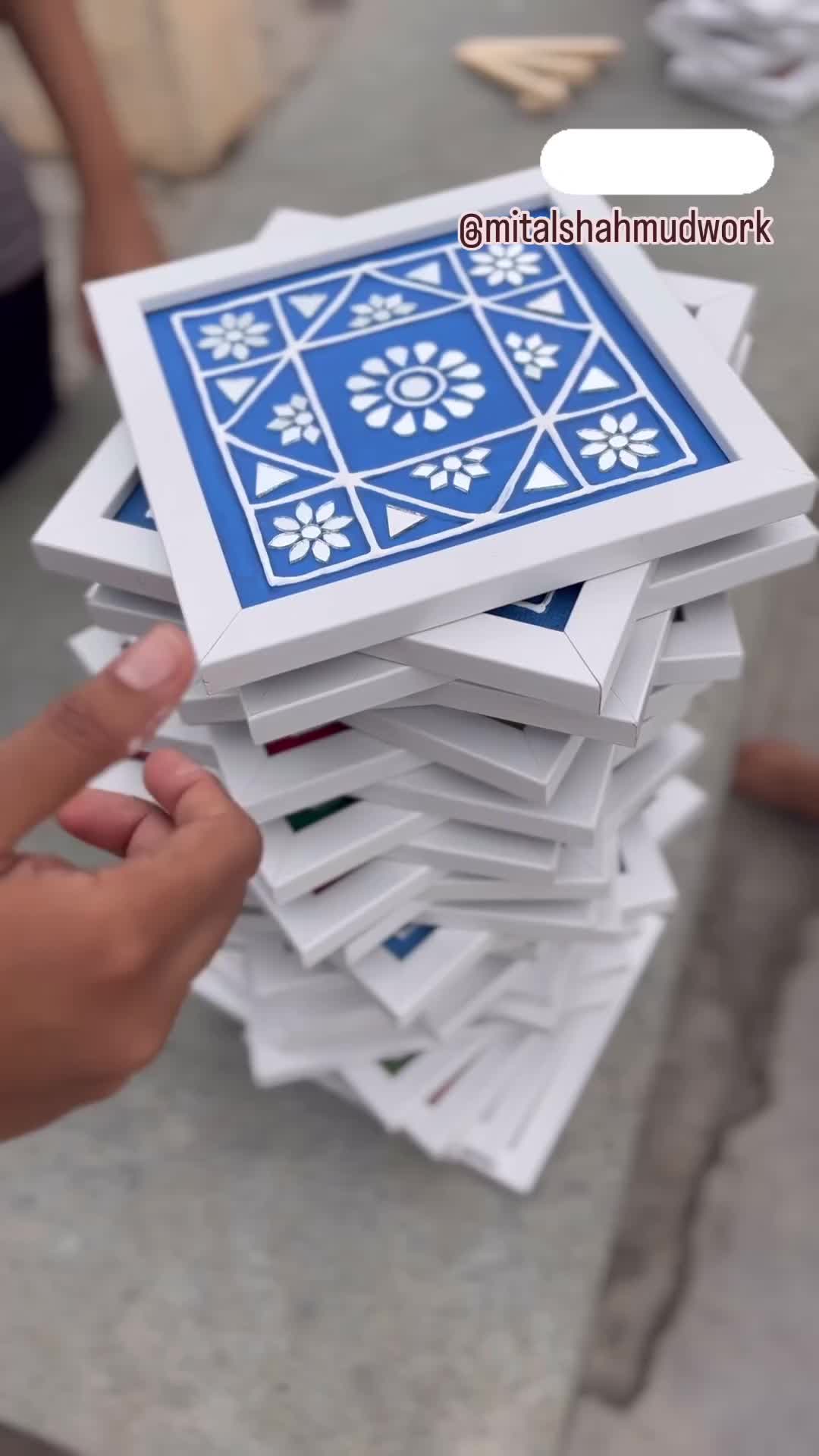 This may contain: a stack of white and blue tiles being held by a person's hand in front of them