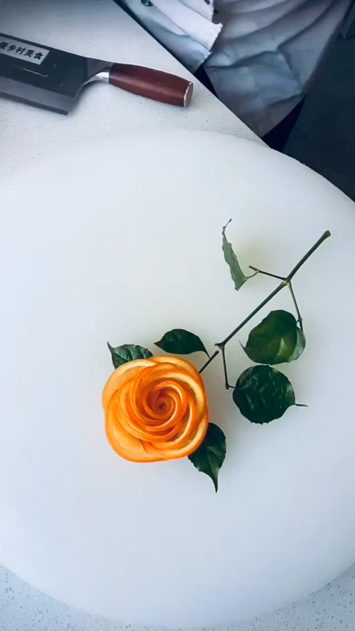 This may contain: a small orange rose sitting on top of a white table