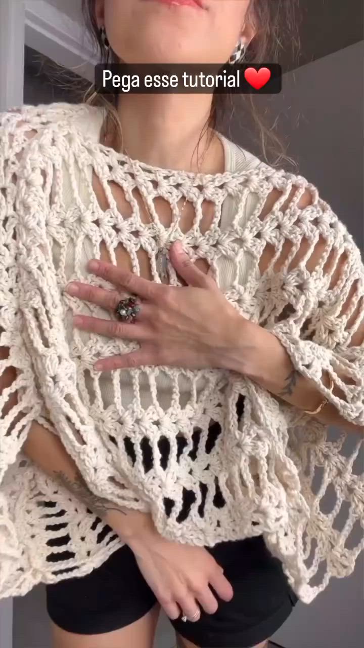 This may contain: a woman with her hands on her chest wearing a white crochet sweater and black shorts