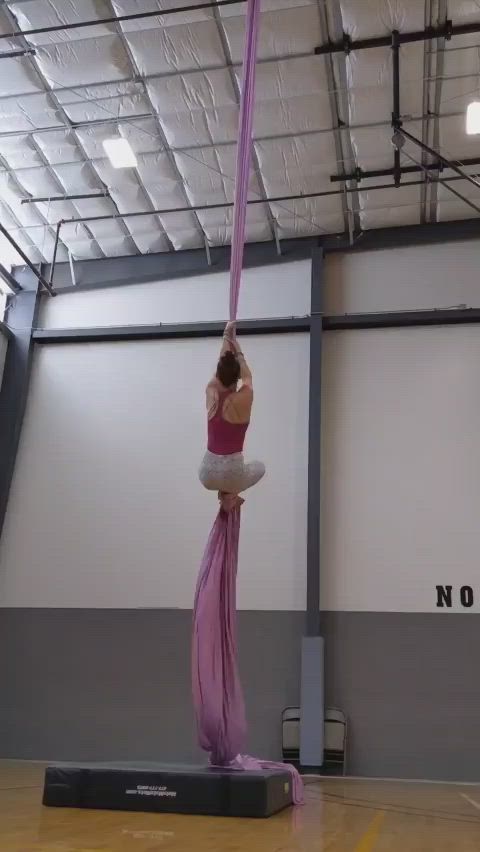 This may contain: a woman is doing aerial acrobatics on a pole in an indoor gym