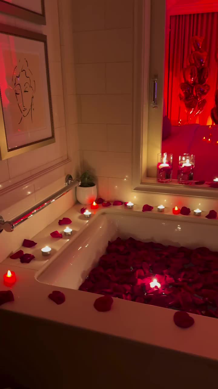 This may contain: a bath tub filled with lots of red rose petals and candles in front of a mirror