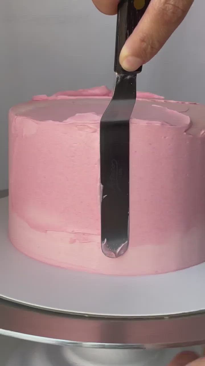 This may contain: a person cutting into a pink cake with a black knife on the top and bottom