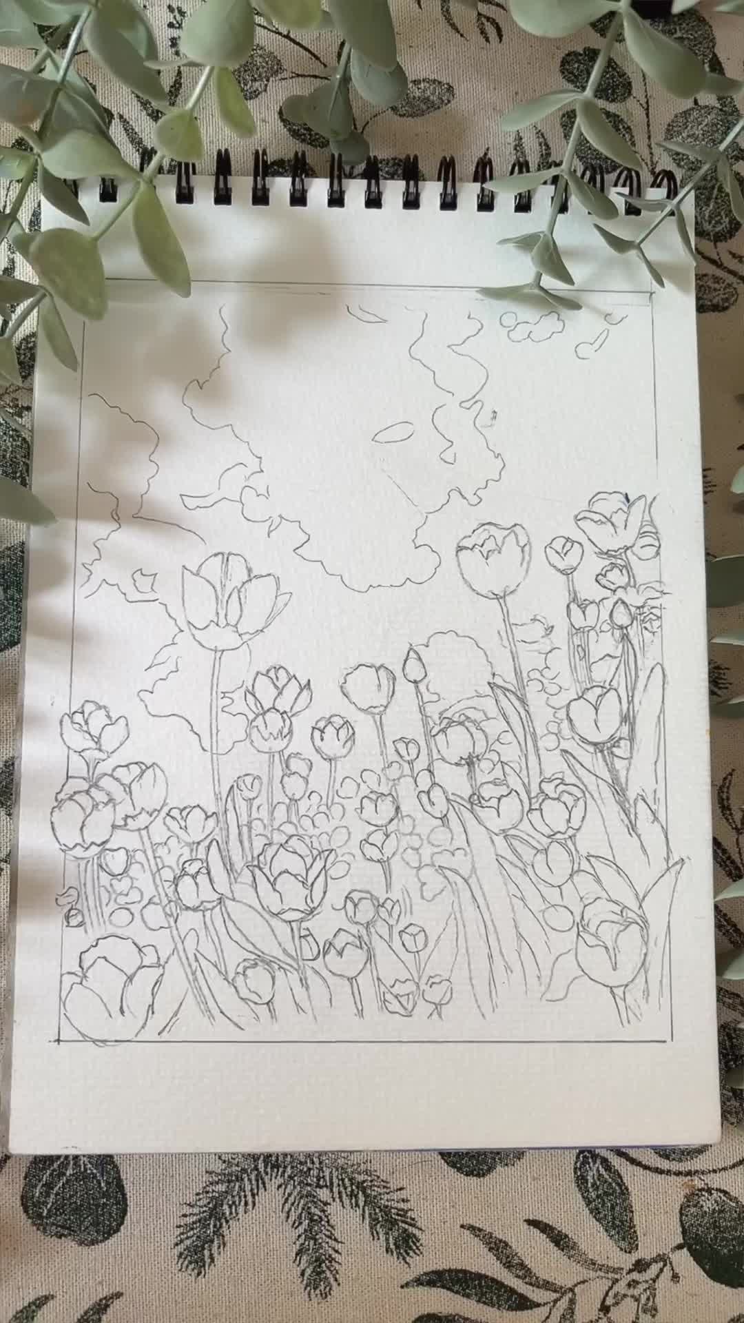 This may contain: someone is holding up a drawing with flowers in the foreground and clouds in the background