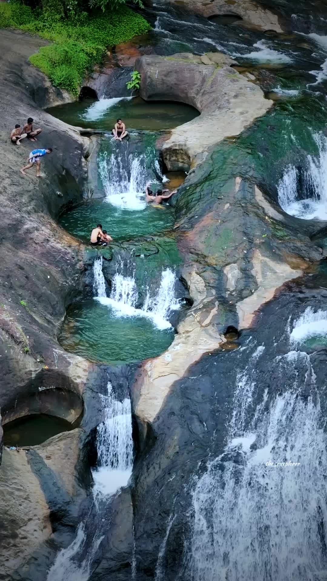 This may contain: people are swimming in the water near some rocks and waterfall cascading, while another person is laying on his stomach