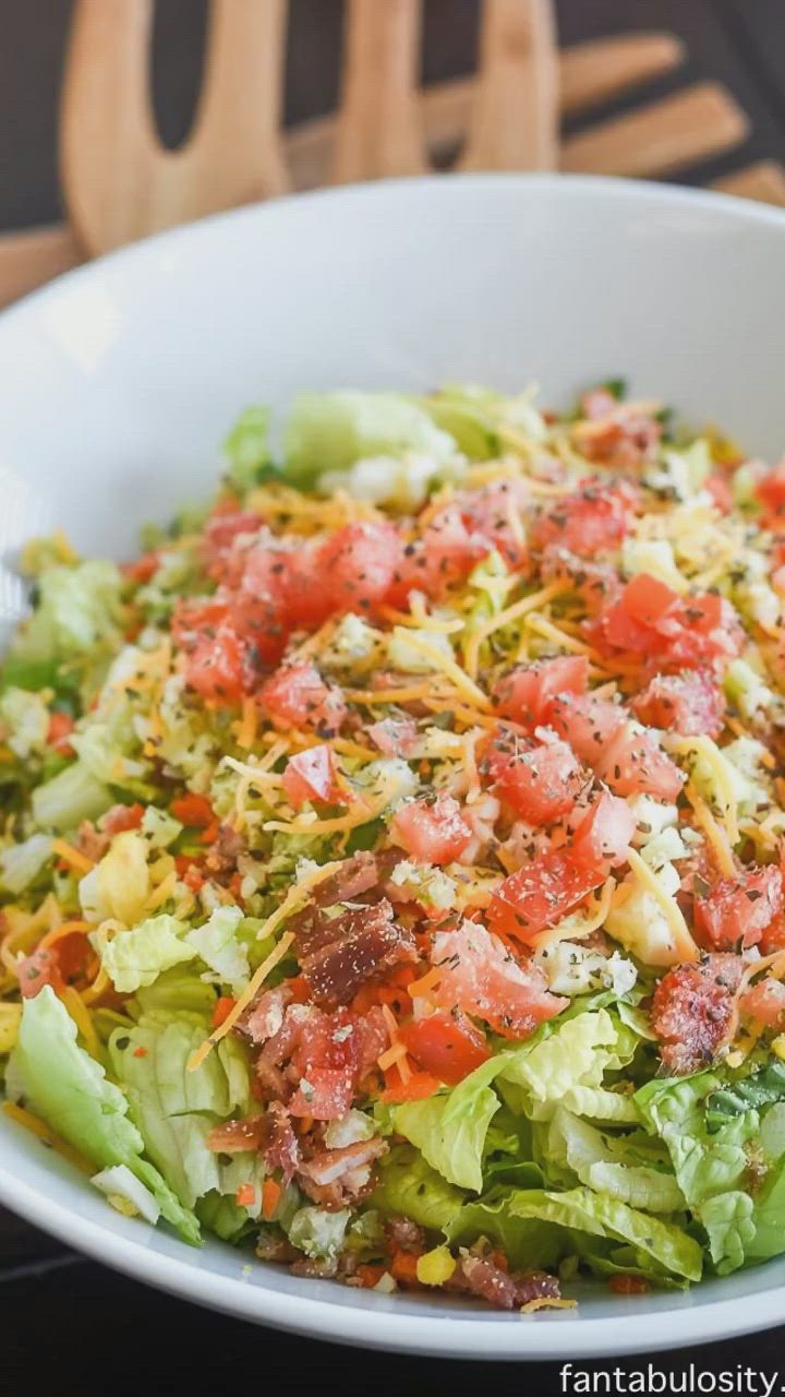 This may contain: a white bowl filled with lettuce, tomatoes and other vegetables on top of a table