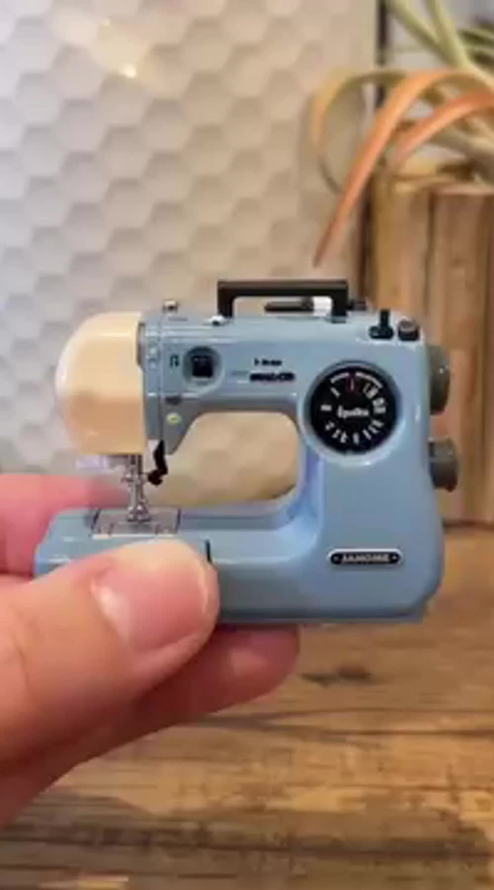 This may contain: someone is holding a miniature sewing machine in their hand