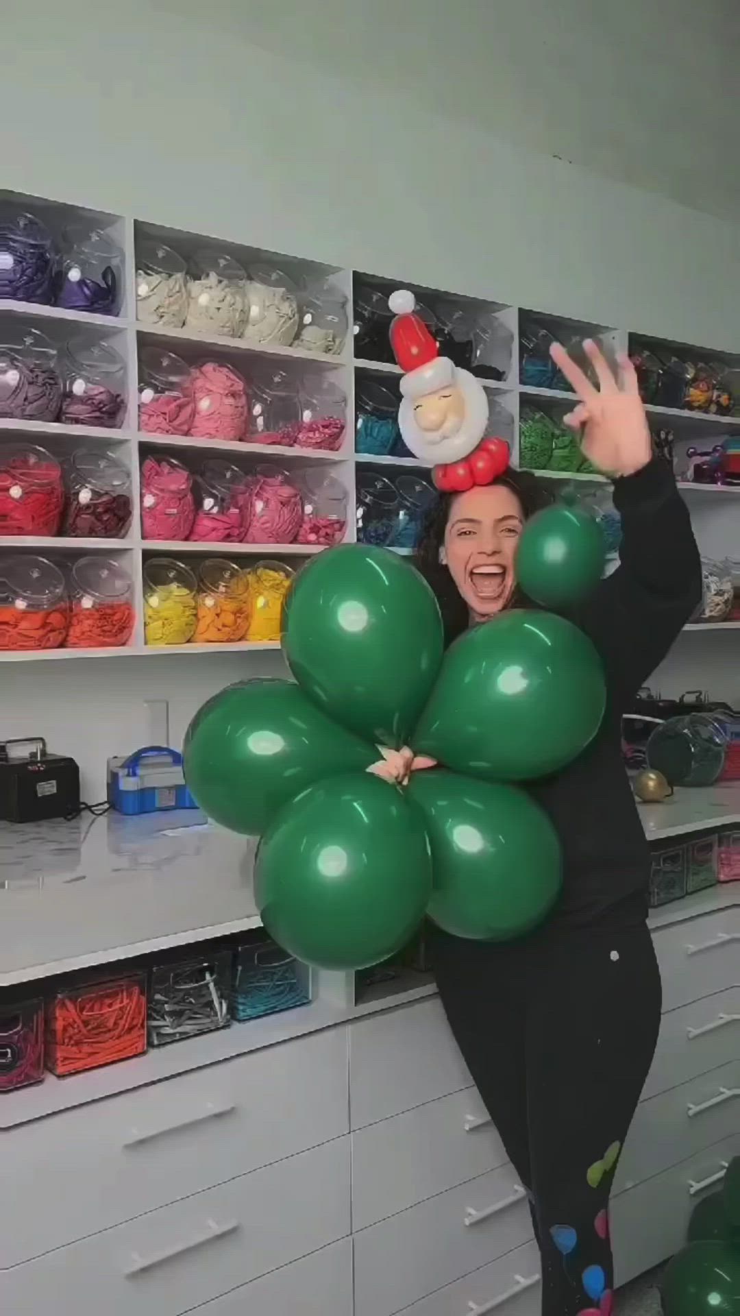 This may contain: a woman is holding up balloons in the shape of a flower and an elf hat