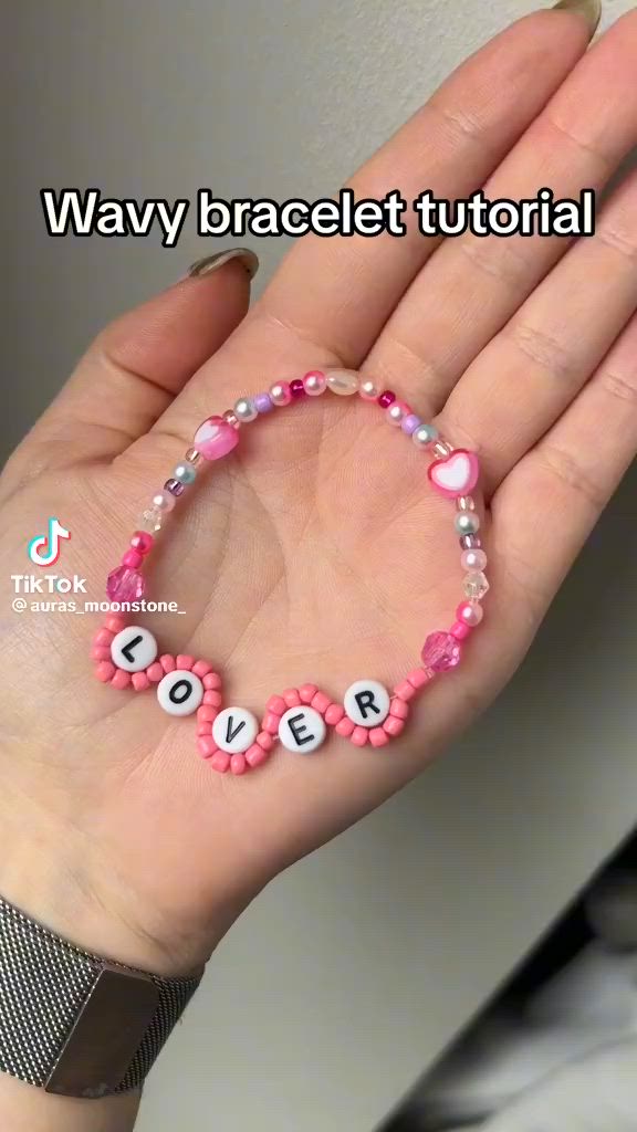 This may contain: a woman's hand holding a pink beaded bracelet with words written on it