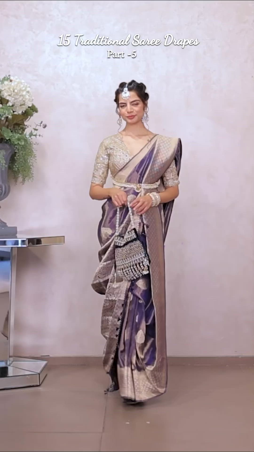 This may contain: a woman in a purple and gold sari standing next to a vase with flowers