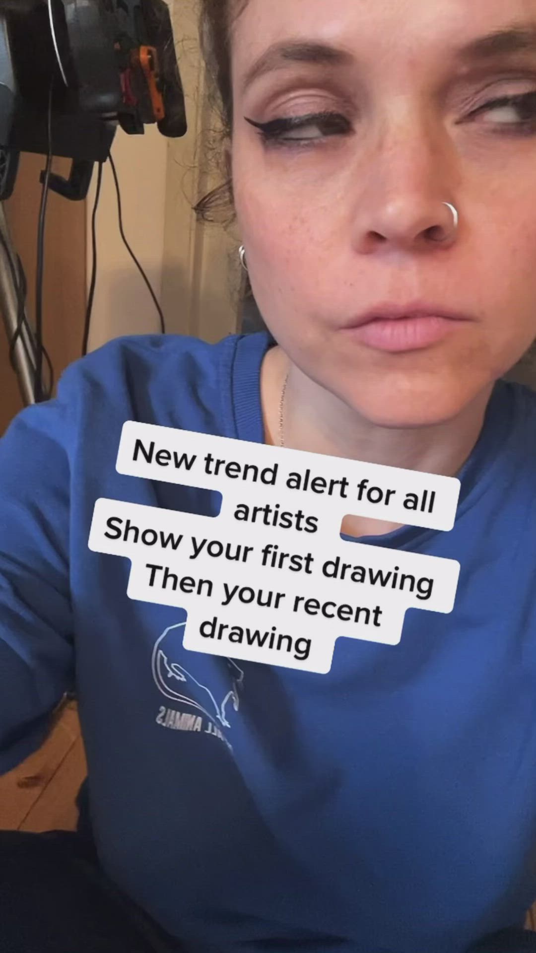 This may contain: a young woman wearing a blue shirt with some stickers on her face that says new trend alert for all artists show your first drawing then your recent drawing