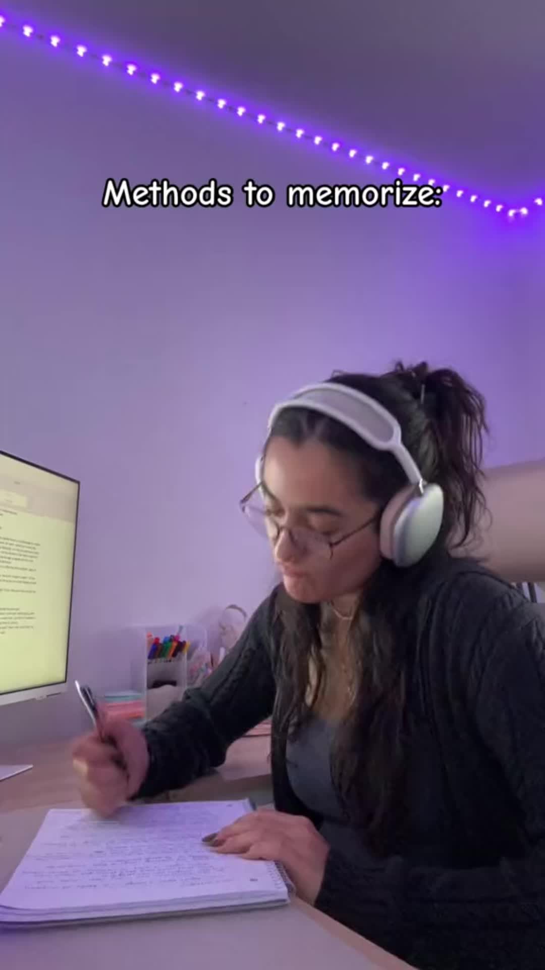 This may contain: a woman sitting at a desk in front of a computer with headphones on and writing