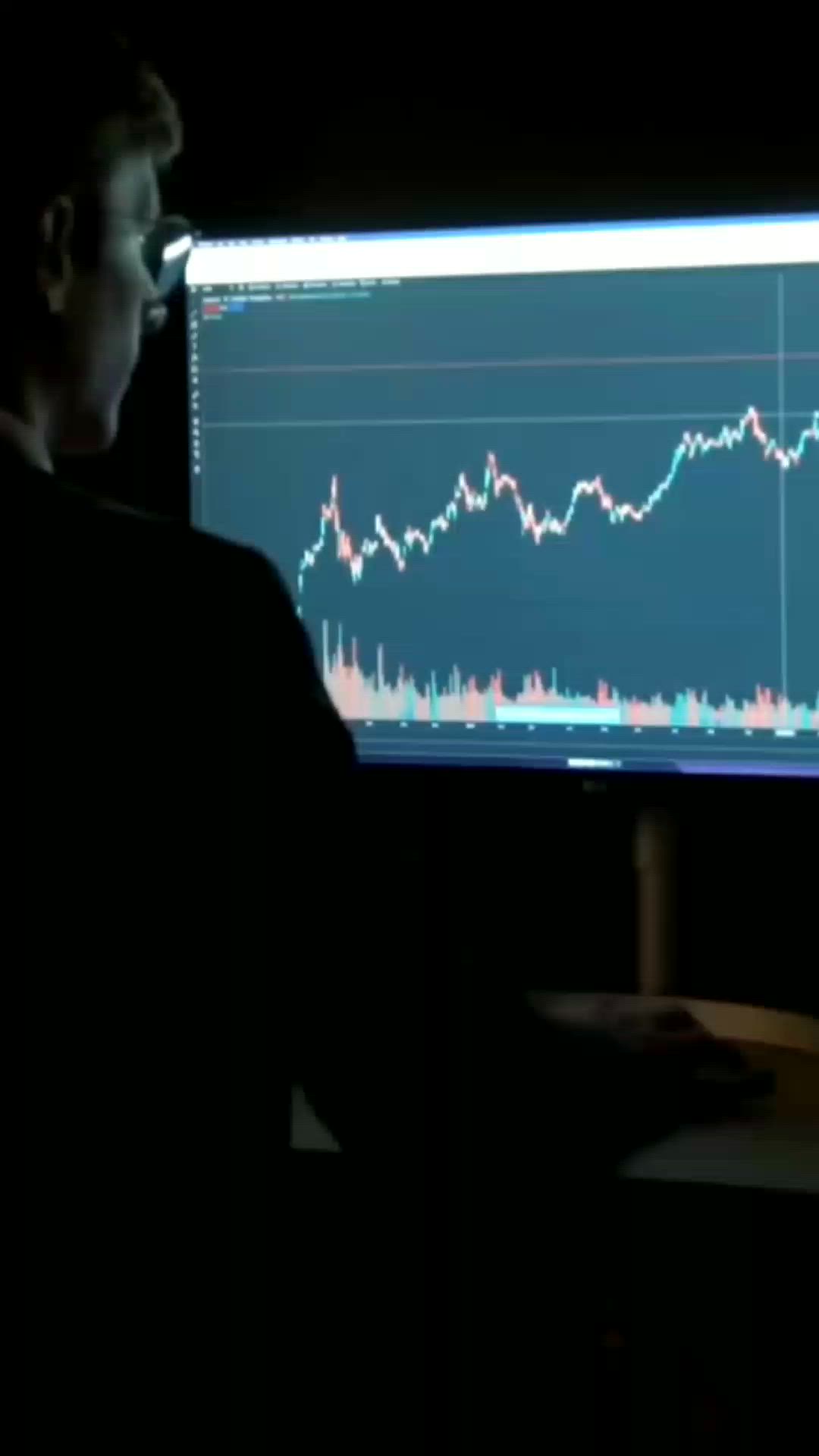 This may contain: a man sitting in front of a computer monitor with a stock market chart on it