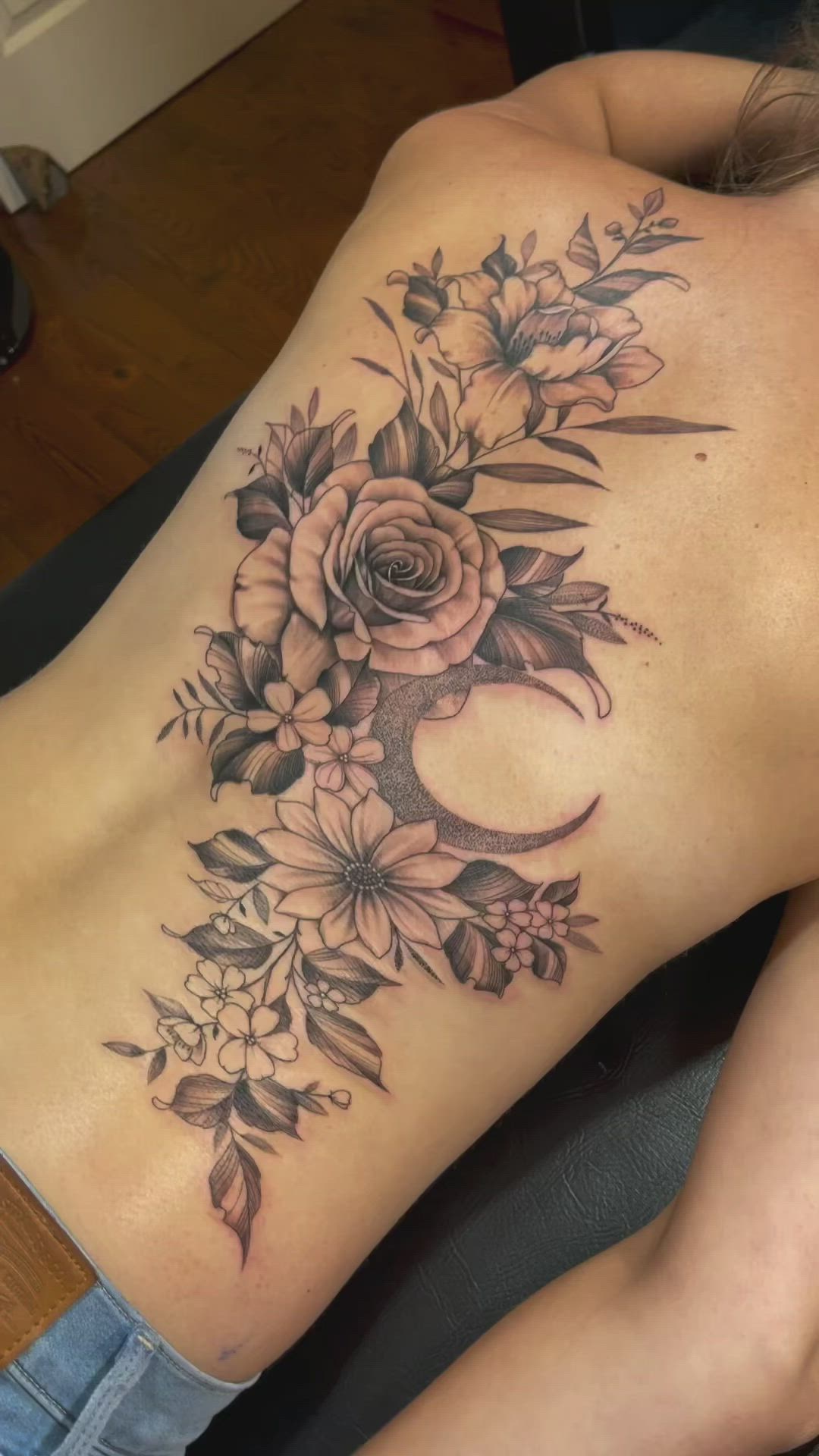 This may contain: a woman's back with flowers on it and a crescent tattoo in the middle